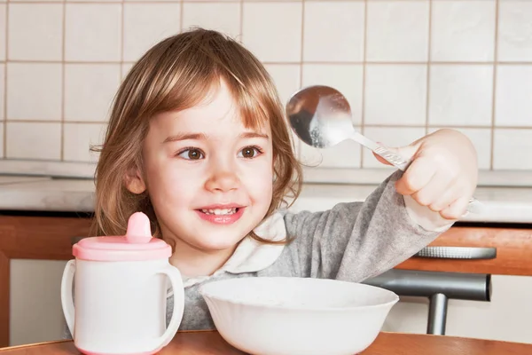 Маленькая девочка ест и пьет за столом на кухне — стоковое фото