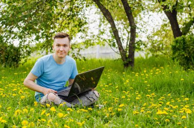 Genç Gyu, yeşil çimenler ve ağaçlar üzerinde dizüstü bilgisayarda çalışıyor..