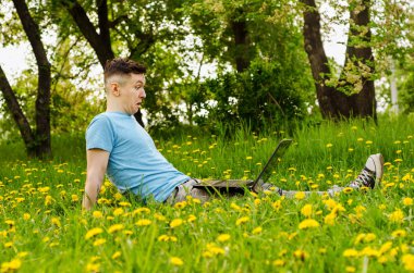Genç Gyu, yeşil çimenler ve ağaçlar üzerinde dizüstü bilgisayarda çalışıyor..