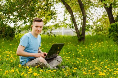 Genç Gyu, yeşil çimenler ve ağaçlar üzerinde dizüstü bilgisayarda çalışıyor..
