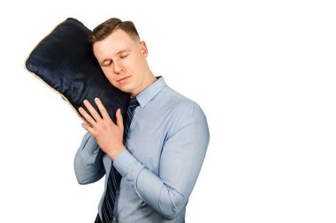 Mavi gömlekli ve kravatlı genç bir işadamı elinde yastıkla uyuyor, beyaz arka planda soyutlanmış.