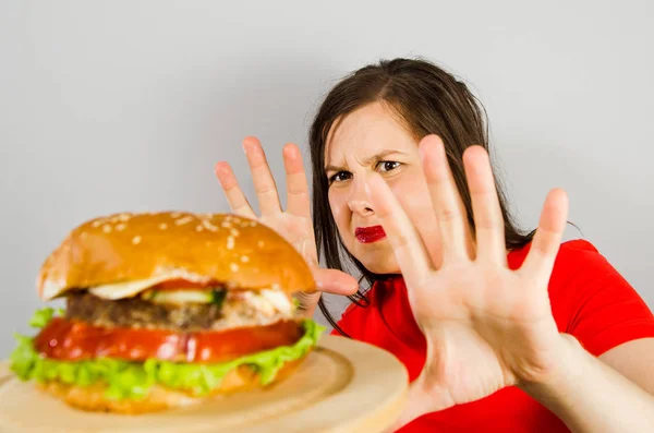 Ung flicka vägrar fett ohälsosam hamburgare eftersom hon går ner i vikt och bantning på grå bakgrund. — Stockfoto