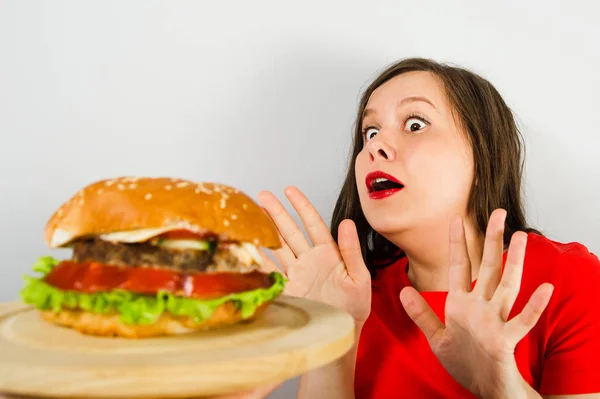 Young girl refuses fat unhealthy hamburger because she is losing weight and dieting on gray background. — 스톡 사진