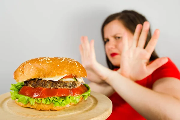 Ung flicka vägrar fett ohälsosam hamburgare eftersom hon går ner i vikt och bantning på grå bakgrund. — Stockfoto