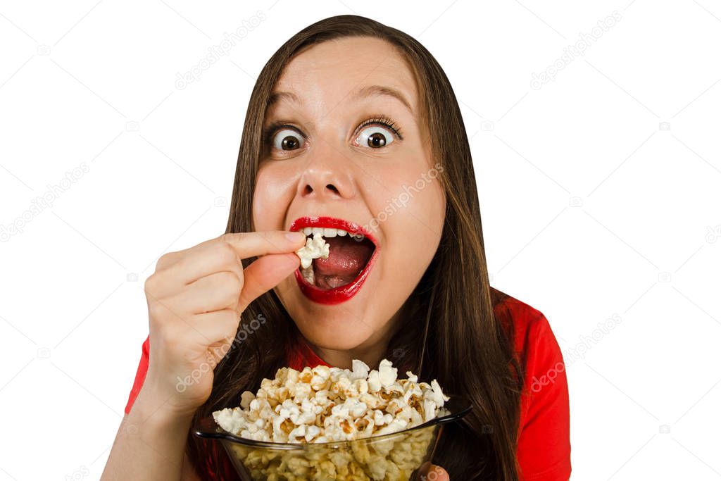 Young pretty girl with opened mouth and wide eyes holds glass bowl with popcorn isolated on white background