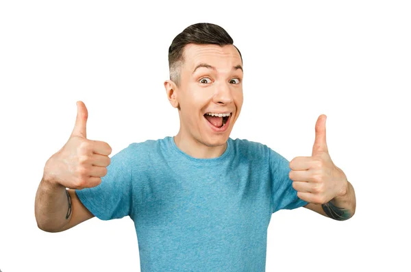 Joven chico sonriente, vestido con una camiseta azul, muestra los pulgares hacia arriba sobre un fondo blanco aislado . — Foto de Stock