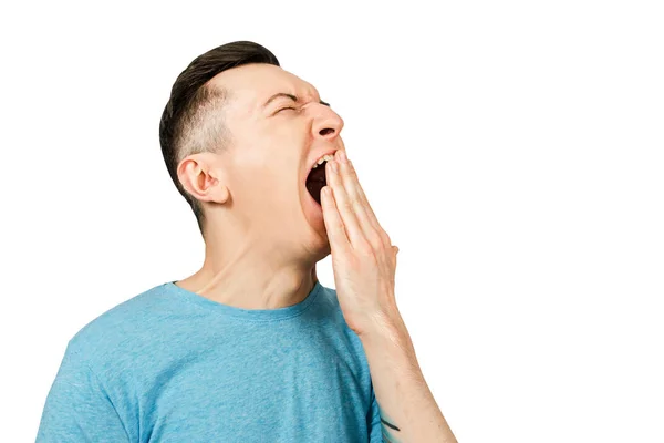 Young yawning guy dressed in a blue t shirt on a isolated white background. Side view. — Stock Photo, Image