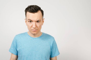 Hafif arka planda mavi tişörtlü kasvetli genç adam..