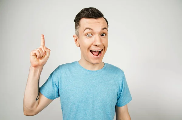 Idea Joven chico sonriente con el dedo en alto, vestido con una camiseta azul sobre un fondo claro . — Foto de Stock