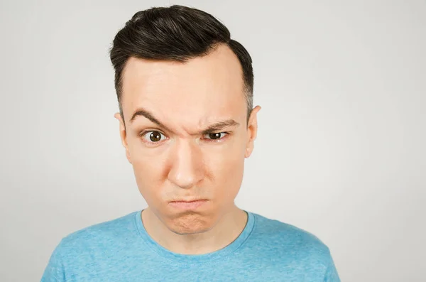 Young gloomy man dressed in a blue t-shirt on a light background. — Stock Photo, Image