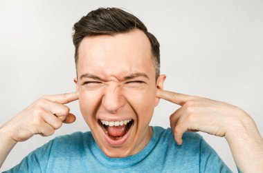 Mavi tişört giyen, kulaklarını kapatan ve arka planda ağlayan genç adam..