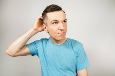 Açık arkaplanda mavi tişört giymiş genç bir adam..