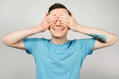 Mavi tişörtlü genç adam, ellerini açık arkaplan üzerine koyarak gözlerini kapattı..