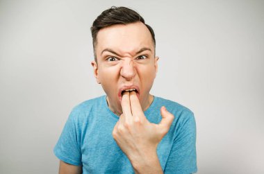 Genç adam kusturmak için iki parmağını ağzına sokuyor, arka planda hafif bir kusma oluyor..