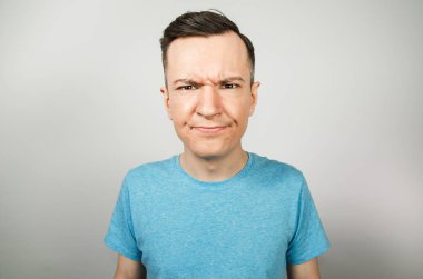 Hafif arka planda mavi tişörtlü kasvetli genç adam.