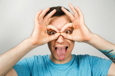 Mavi tişörtlü genç adam, arka planda, avucunun içinden dürbünle bakıyor. Yakın plan portre