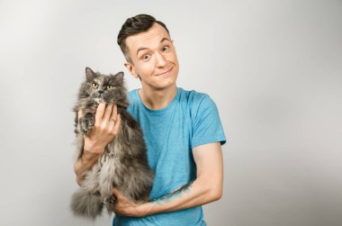 Genç adam açık gri arka planda gri Britanya kedisi tutuyor.