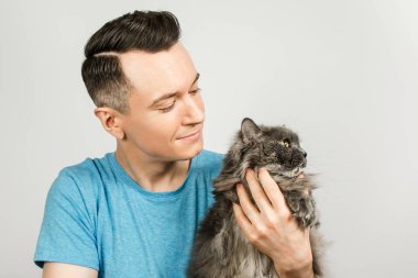 Genç adam açık gri arka planda gri Britanya kedisi tutuyor.