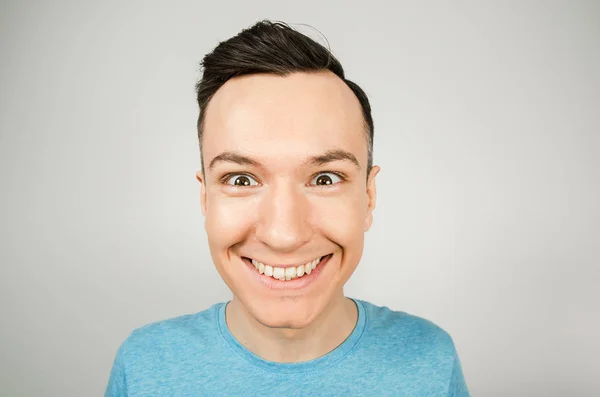 Close-up portret van jong gelukkig glimlachen guy, gekleed in een blauw t-shirt op een lichte achtergrond. — Stockfoto
