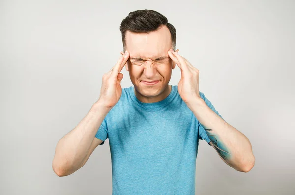 Tipo tiene dolor de cabeza, migraña vestida con una camiseta azul sobre un fondo claro . — Foto de Stock