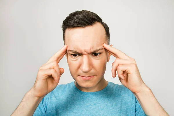 Young thinking man dressed in a blue t-shirt on a light background. — Stock Photo, Image