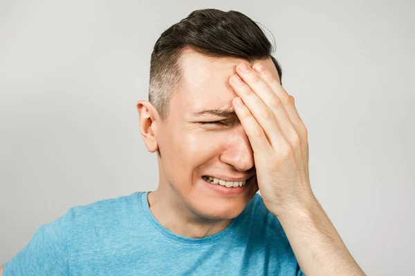 Young crying guy cover face with hands with open mouth, dressed in a blue t shirt on a light background. — Stock Photo, Image