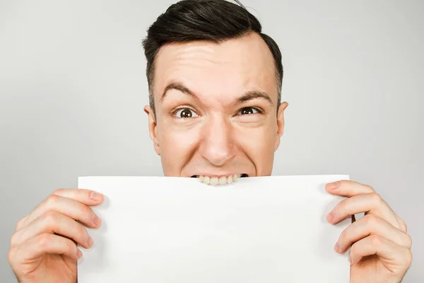 Gars mord et déchire avec ses dents une feuille blanche de papier A4 sur un fond clair — Photo