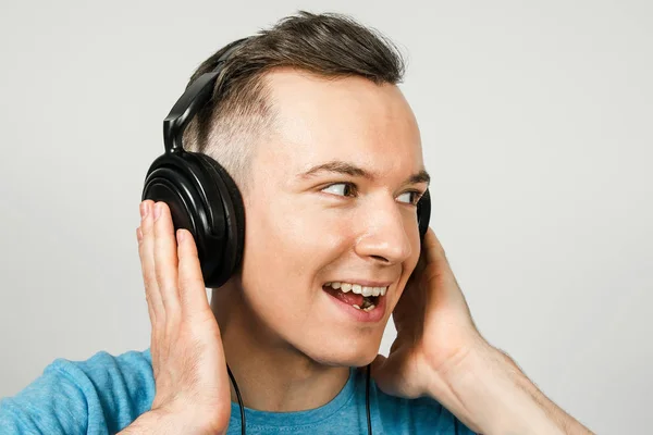 Ung rolig kaukasier kille i blå t-shirt lyssna på musik på hörlurar på ljusgrå bakgrund. — Stockfoto