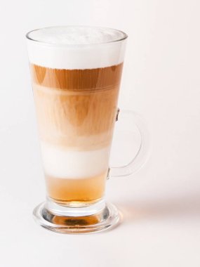 Şeffaf bir fincanda kahve kapuçinosu ve beyaz bir fonda çay tabağı.