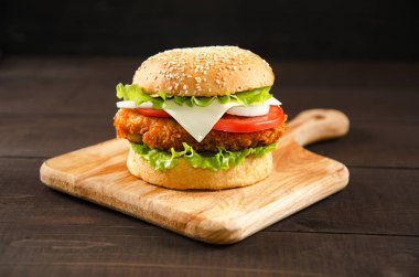 Hamburger tahta bir arka planda kesme tahtasının üzerinde yatıyor..