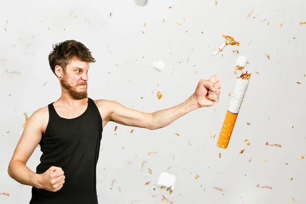 Νεαρός γενειοφόρος χτυπάει τη γροθιά του σε ένα τσιγάρο, σε λευκό φόντο. Έννοια της καταπολέμησης του καπνίσματος — Φωτογραφία Αρχείου