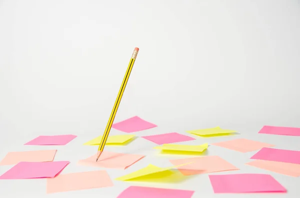 Růžové a žluté samolepky pod zápisníkem, na kterém je napsána tužka, která visí ve vzduchu na světlém pozadí. — Stock fotografie