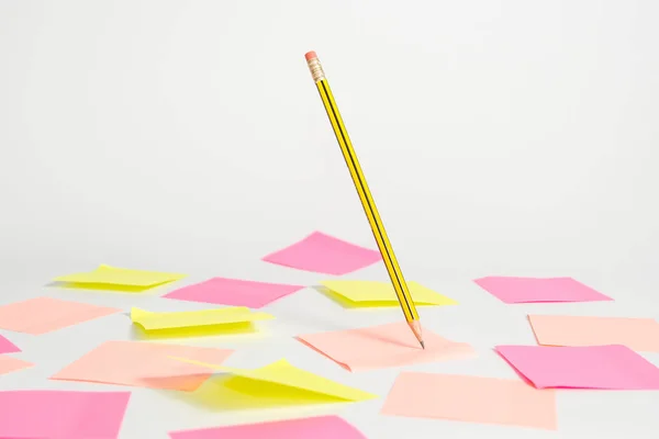 Růžové a žluté samolepky pod zápisníkem, na kterém je napsána tužka, která visí ve vzduchu na světlém pozadí. — Stock fotografie