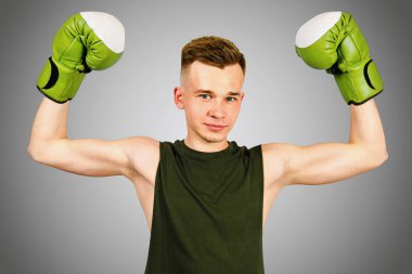 Gri arka planda yeşil boks eldivenli genç adam..