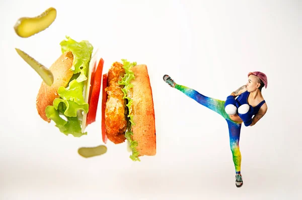 A young girl kick a hamburger. The concept is the fight against unhealthy food. — Stock Photo, Image