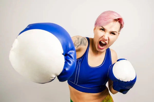 Belle jeune femme en gants de boxe bleus boxe sur un fond clair . — Photo