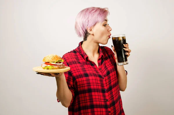 Ung vacker flicka håller burgare och glas cola, på en vit bakgrund. — Stockfoto