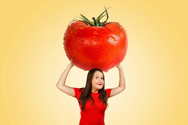 Bonito engraçado jovem menina segura sobre si mesma enorme tomate vermelho com gotas de água no fundo laranja — Fotografia de Stock