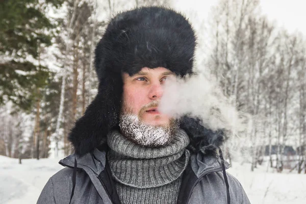 Hombre ruso siberiano con barba en la escarcha en el frío helado en el invierno se congela y lleva un sombrero con una orejera . — Foto de Stock