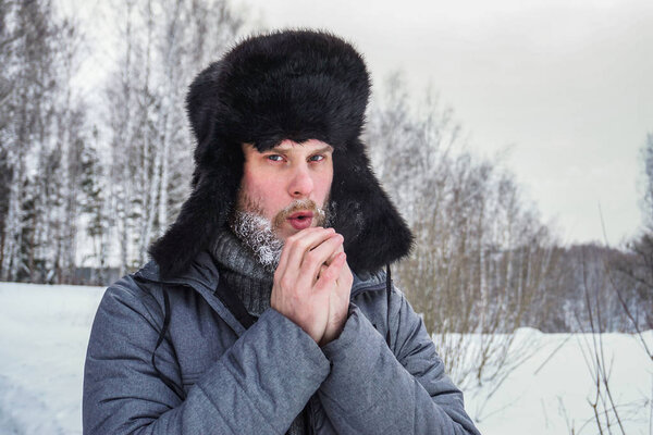 Siberian Russian man with a beard in hoarfrost in freezing cold in the winter freezes and wears a hat with a earflap.