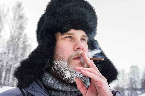 Hombre ruso siberiano con barba en la escarcha en el frío helado en el invierno se congela y lleva un sombrero con una orejera . — Foto de Stock