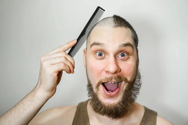 half trimmed bald guy on isolated background. man hold comb and clipper. Concept of hair loss, alopecia, transplantation