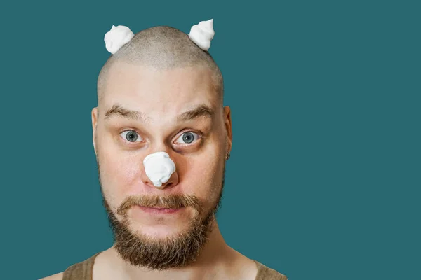 Ein Typ mit Bart, Schaum und Gel im Gesicht bereitet sich darauf vor, sich morgens zu Hause auf farbigem Hintergrund zu rasieren. — Stockfoto