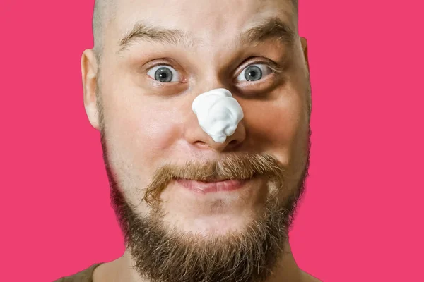 Um cara com uma barba com espuma e gel em seu rosto está se preparando para se barbear de manhã em casa em um fundo colorido . — Fotografia de Stock