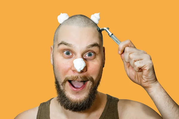 Um cara com barba e navalha na mão, com espuma e gel no rosto, faz a barba pela manhã em casa. — Fotografia de Stock