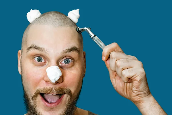 Um cara com barba e navalha na mão, com espuma e gel no rosto, faz a barba pela manhã em casa. — Fotografia de Stock