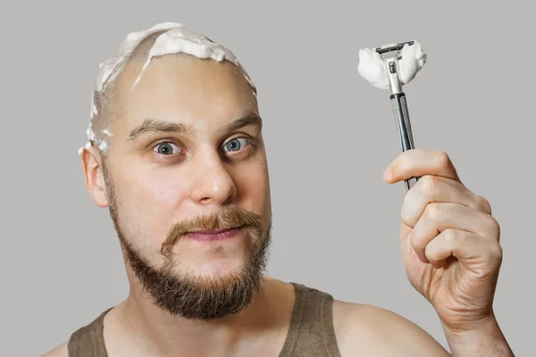 Een man met een baard en een scheermes in zijn hand, met schuim en gel op zijn gezicht scheert zich 's morgens thuis — Stockfoto