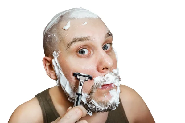 A guy with a beard and a razor in his hand, with foam and gel on his face shaves in the morning at home — 스톡 사진