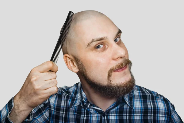 Homem barbudo careca com barba e pente na mão pentes contra um fundo isolado — Fotografia de Stock