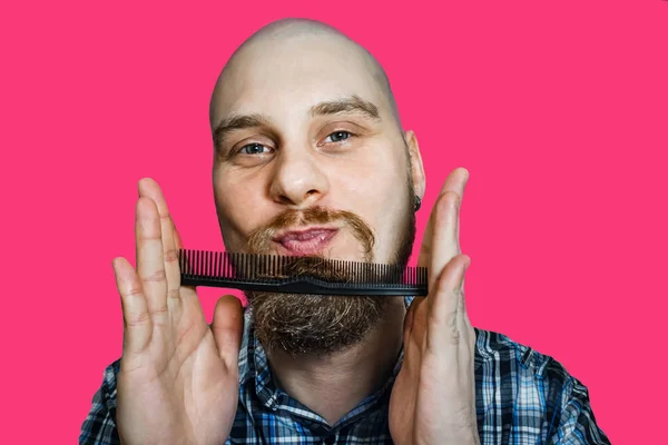 Homem barbudo careca com barba e pente na mão pentes contra um fundo isolado — Fotografia de Stock